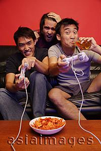 Asia Images Group - Three young men, with video games, beer and chips