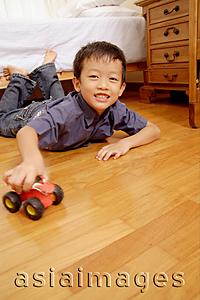 Asia Images Group - Young boy lying on floor with toy, looking at camera