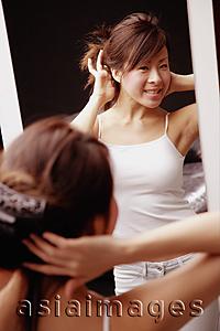 Asia Images Group - Young woman looking at mirror touching her hair