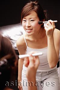 Asia Images Group - Young woman looking at mirror applying blusher with brush