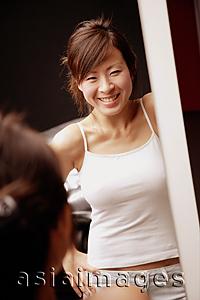 Asia Images Group - Young woman looking at mirror, hands on hips