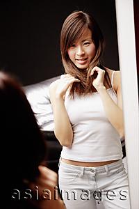Asia Images Group - Young woman looking at mirror, touching her hair