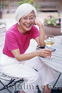 Asia Images Group - Mature woman sitting outdoors with wine glass, looking at camera