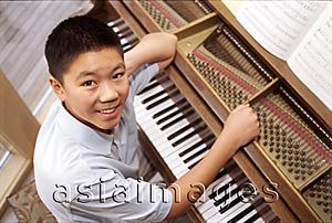 Asia Images Group - Boy sitting at piano, looking up at camera