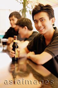 Asia Images Group - Young man at bar counter with beer bottle, people in the background