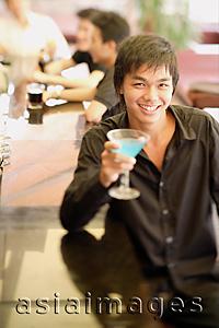 Asia Images Group - Young man at bar counter holding cocktail, people in the background