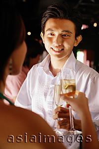 Asia Images Group - Couple at night club, holding champagne glasses, man facing woman
