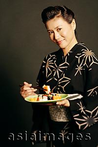 Asia Images Group - Woman in Japanese costume, holding chopsticks and a plate of Japanese food