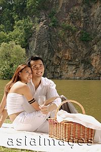 Asia Images Group - Couple sitting by a lake, with picnic basket, looking away
