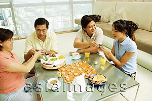 Asia Images Group - Family sitting in living room with food and board game on table in front of them.