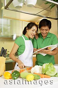 Asia Images Group - Couple in kitchen, looking through cookbook