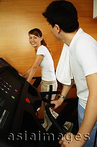 Asia Images Group - Couple in gym using treadmill, looking at each other