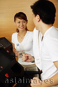 Asia Images Group - Couple in gym, man on treadmill, woman holding bottle of water looking at him