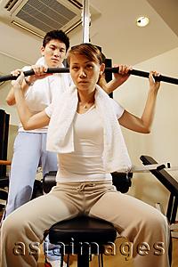 Asia Images Group - Couple in gym, man helping woman with exercise machine