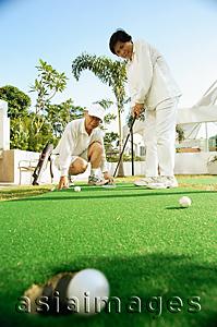 Asia Images Group - Senior couple playing golf, woman with golf club, man crouching down