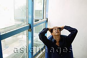 Asia Images Group - Man sitting on chair, hands on head