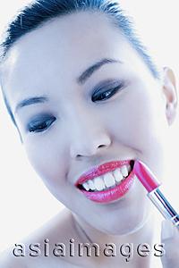 Asia Images Group - Woman applying lipstick, smiling and looking down