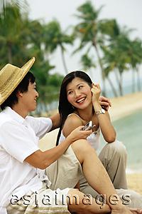 Asia Images Group - Couple sitting on beach, man holding mobile phone