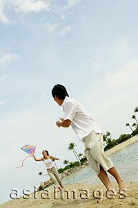 Asia Images Group - Couple flying kite along beach, man turning to look at woman