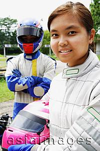 Asia Images Group - Young woman in sports jumpsuit, holding helmet, looking at camera, man behind her
