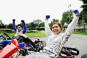 Asia Images Group - Young man and woman in go-carts, hands outstretched, smiling at camera