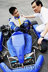 Asia Images Group - Young man in go-cart, father crouching down next to him
