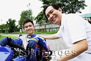 Asia Images Group - Young man in go-cart, father crouching down next to him, both looking at camera