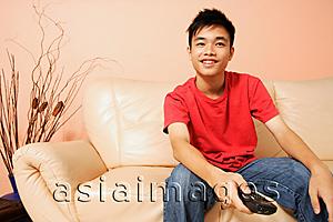 Asia Images Group - Teenage boy sitting on sofa, holding remote control