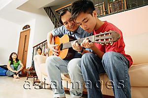 Asia Images Group - Father teaching son to play guitar, mother and daughter in the background
