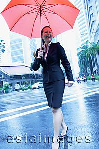 Asia Images Group - Business woman holding umbrella, walking across the road