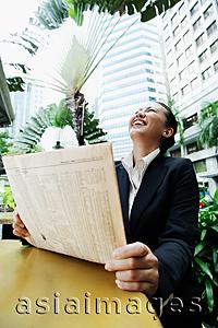 Asia Images Group - Business woman holding newspaper, looking up