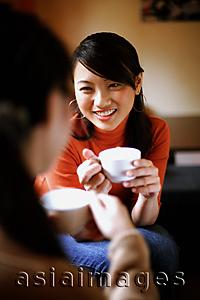 Asia Images Group - Two young women drinking from cups, face to face, over the shoulder view