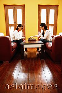 Asia Images Group - Young women sitting in living room, playing chess