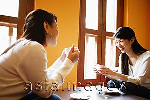 Asia Images Group - Two young women, sitting face to face, holding cups of coffee