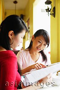Asia Images Group - Young women in cafe, looking at newspaper together, sitting side by side