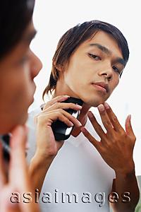 Asia Images Group - Young man looking at mirror, shaving with electric shaver
