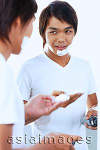 Asia Images Group - Young man with shaving foam on face, looking at reflection in mirror