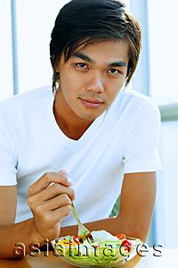 Asia Images Group - Young man looking at camera, bowl of salad in front of him