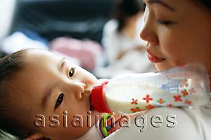 Asia Images Group - Baby girl drinking from bottle, mother carrying her