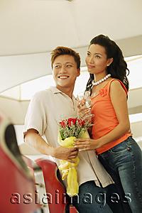 Asia Images Group - Couple standing, man holding bouquet, woman holding wine glass