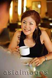 Asia Images Group - Couple in cafe, woman holding cup, looking at man across from her