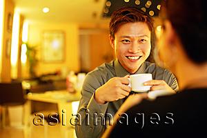 Asia Images Group - Couple in restaurant, man holding cup, facing woman, over the shoulder view