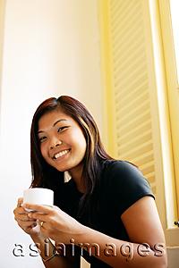 Asia Images Group - Young woman holding cup of coffee, looking at camera, smiling