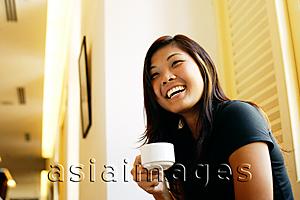 Asia Images Group - Young woman holding cup of coffee, looking away, smiling
