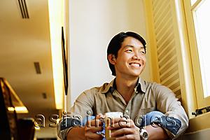 Asia Images Group - Man sitting, holding mug of coffee, smiling