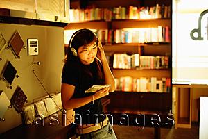Asia Images Group - Young woman standing, listening to music, holding CD
