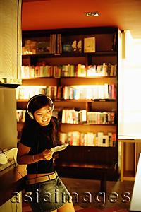 Asia Images Group - Young woman standing, listening to music, holding CD, smiling