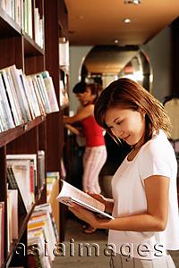 Asia Images Group - Young woman at bookstore, reading book