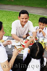 Asia Images Group - Family sitting at picnic table, father passing daughter food