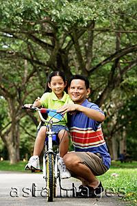 Asia Images Group - Girl on bicycle, father crouching down next to her, both looking at camera